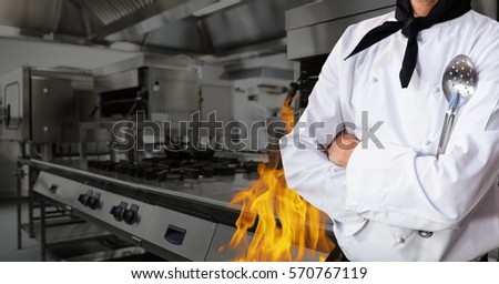 Mid section of chef standing with arms crossed in kitchen of restaurant