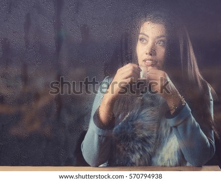Young female with a cup of coffee looking out through the steamy window.