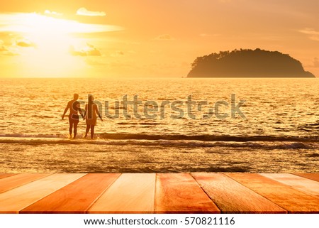 Wood plank with silhouette of couple on the beach against sunset. Summer concept.