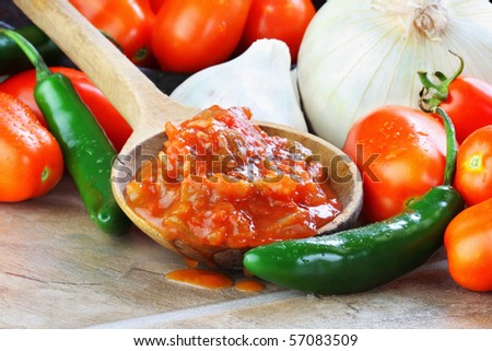 Rustic wooden spoon filled with spicy fresh salsa, surrounded by freshly picked and washed ingredients.