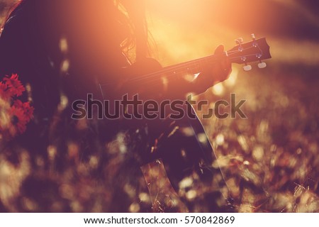 Silhouette Beautiful girl relax by playing acoustic guitalele on the flower grass fieid with flower basket at sunset. vintage color effect