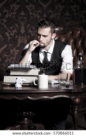 A young man sits on a leather armchair, at a vintage wooden table. He wears a white shirt, a black vest, a black tie. He keeps a cigarette in his fingers and smokes while thinking on his writings.  Royalty-Free Stock Photo #570866011