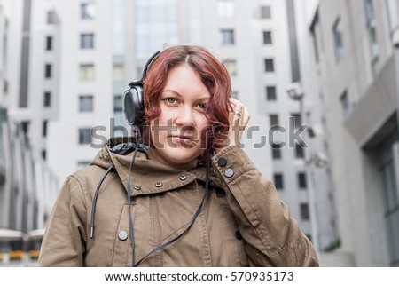Young red-haired woman listening to music in big headphones on the street
