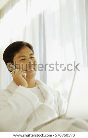 Young man wearing robe, using laptop and using mobile phone