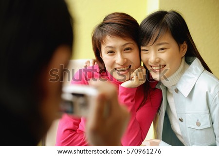 Young man holding camera, two women posing for picture