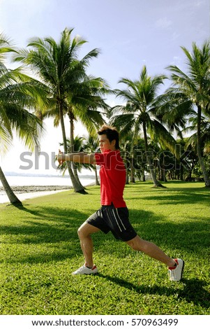 Man stretching in park, wearing red shirt