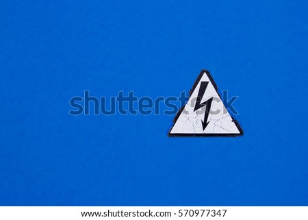 Cracked triangular sign high voltage on blue wall closeup