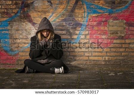 runaway girl thinks and sits in front of a wall with graffiti Royalty-Free Stock Photo #570983017