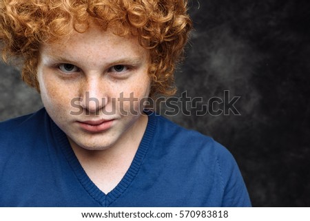 Cropped Studio portrait of curly red-haired freckled teenager in blue shirt