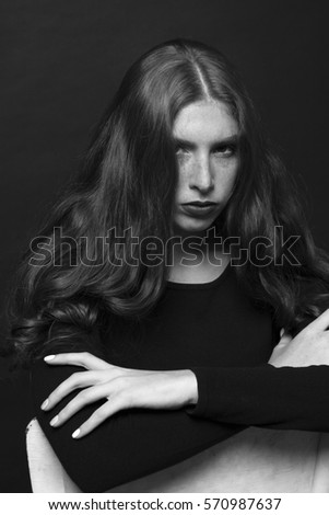 Black and white portrait of a sad girl dressed in black blouse. Girl with long curly hair. Gentle make-up and beautiful freckles.