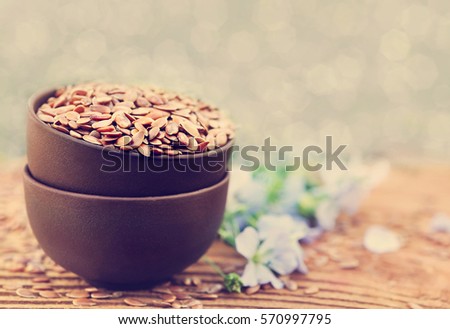 Flax seeds in bowl on blue linum plants and linseeds background, selective focus, shallow DOF, toned