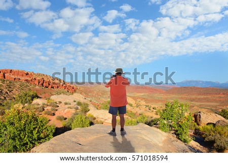 Man standing on top of the mountain taking photos ,looking at beautiful autumn mountains landscape. Moab, Utah, Arches National Park.