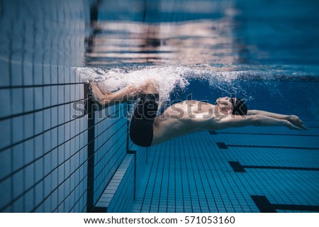 Shot of fit young man turning over underwater. Pro male swimmer in action inside swimming pool.