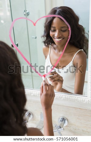 Beautiful young woman drawing big heart on mirror with lipstick