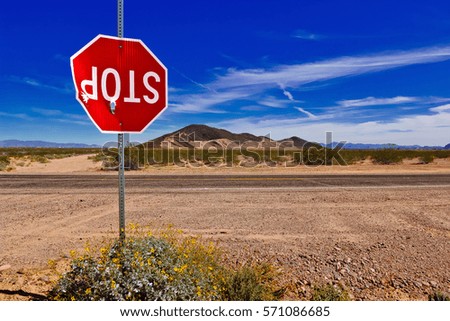 A Stop Sign in a remote area of Arizona, vandalized and shot up to the point of barely hanging onto its pole.