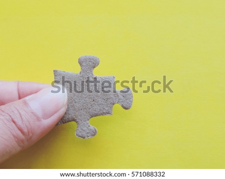 hand holding a puzzle piece on yellow background.          