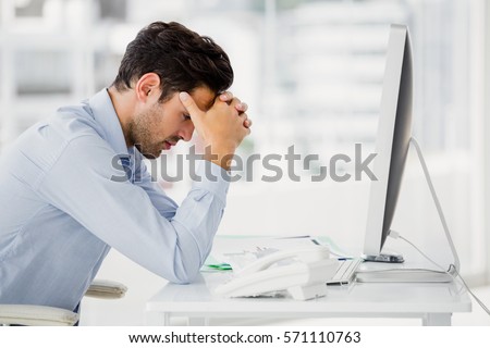 Frustrated businessman sitting on desk with hand on head in office Royalty-Free Stock Photo #571110763