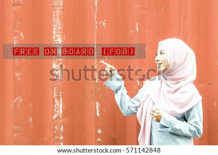The beautiful Malaysian young with muslimah attire lady pointing her finger to the words Free on Board (FOB)  . A logistic terms for shipping and forwarding with scratch container background.  