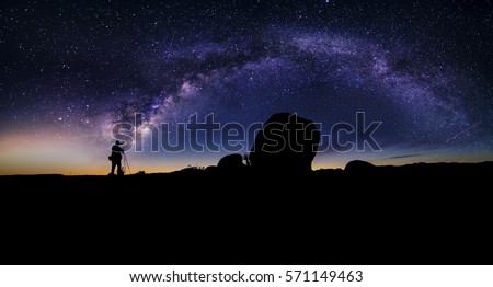 Photographer doing astro photography in a desert nightscape with milky way galaxy.  The background is stary celestial bodies in astronomy.  The heaven depicts science and the divine. Royalty-Free Stock Photo #571149463