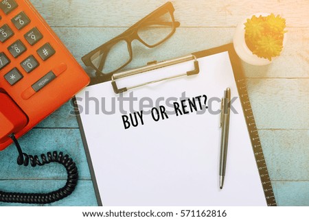 Top view of clipboard and white sheet written with BUY OR RENT on blue wooden background. Business Concept.