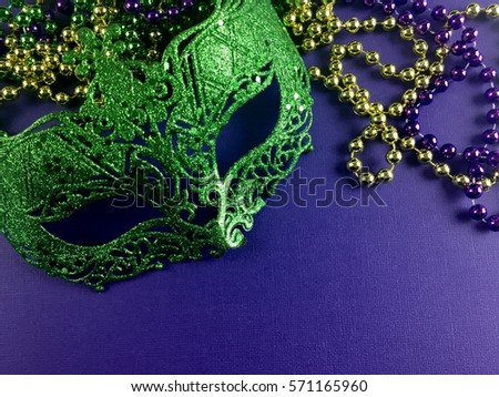 Green Mardi Gras mask and beads on a purple background