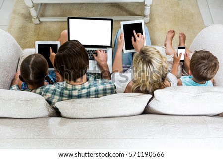 Overhead view of family using various technologies while sitting on sofa at home Royalty-Free Stock Photo #571190566
