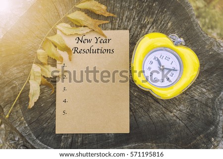a sheet of writing paper, dried leaves and clock on the wooden table