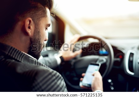 Man looking at mobile phone while driving a car. Royalty-Free Stock Photo #571225135