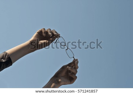 Human hands holding eye glasses against blue sky. Concept of Knowledge and education.