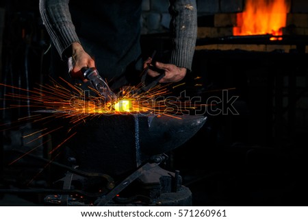 The blacksmith manually forging the molten metal on the anvil in smithy with spark fireworks Royalty-Free Stock Photo #571260961