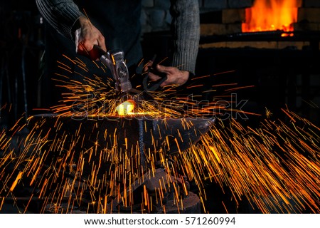 The blacksmith manually forging the molten metal on the anvil in smithy with spark fireworks Royalty-Free Stock Photo #571260994