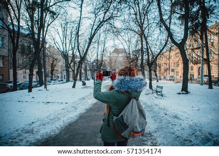 Redhead girl with long hair walking through the old european city. Traveler with a funny backpack. Winter vacation in Lvov city. Colorful lifestyle