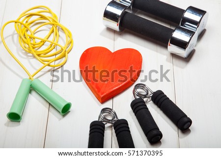 Heart, dumbbells, skipping rope and the expander on a white wooden background