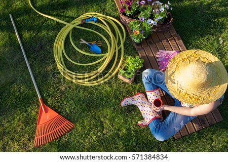 Woman having a coffee break while working in the garden, gardening tools around. Royalty-Free Stock Photo #571384834