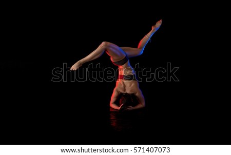 woman athlete gymnast performing acrobatic elements on a black background in the scenic red and blue light.