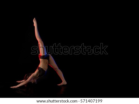 woman athlete gymnast performing acrobatic elements on a black background in the scenic red and blue light.