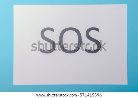 Word SOS written on white paper. Blue background