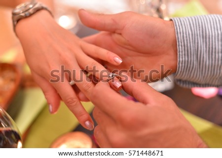 Male hands putting ring on finger of woman  restaurant dinner