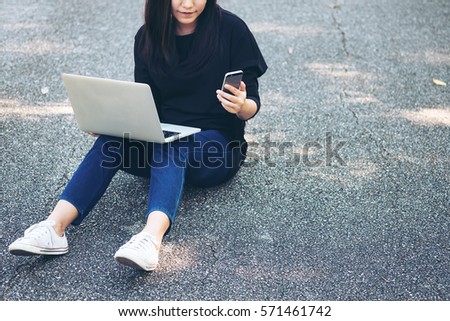A woman sitting on the road and using laptop and smartphone 