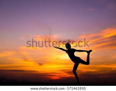 Silhouette of young woman practicing yoga on the roof with beautiful sunset background.