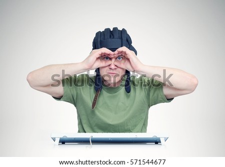 Man in a tank helmet looks through fingers like binoculars