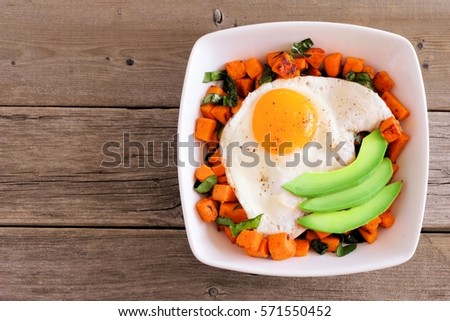 Breakfast nutrient bowl with sweet potato, egg, avocado and spinach overhead view on rustic wood