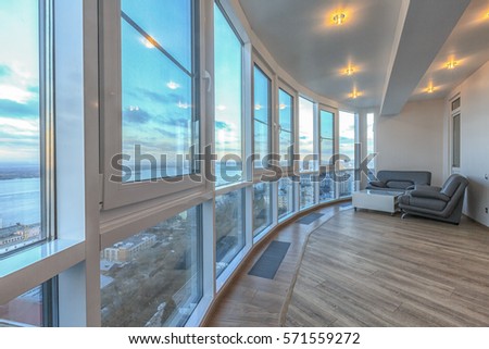 Contemporary balcony with panoramic windows and fabulous view. Hardwood floor. White ceiling. Luxury apartment with expensive designer materials. Royalty-Free Stock Photo #571559272