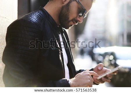 Cropped image of stylish man in sun glasses typing text message on smartphone while using 4G high speed internet connection, hipster guy looking news in social network, copy scape for advertising