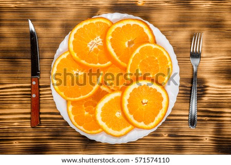dish of sliced oranges on burnt wooden desk with fork and knife. food pattern