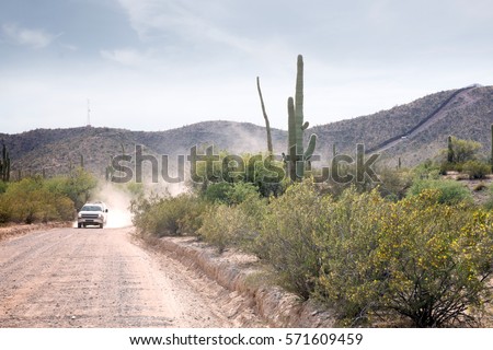  The border between the US states and Mexico. Border control is going on the road along the fence Royalty-Free Stock Photo #571609459
