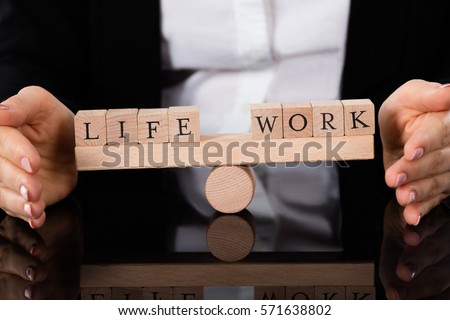 Businesswoman Hand Covering Balance Between Life And Work On Seesaw At Table