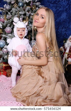 holiday photo of beautiful family. Gorgeous mother with long blond hair posing with adorable cute daughter beside Christmas tree