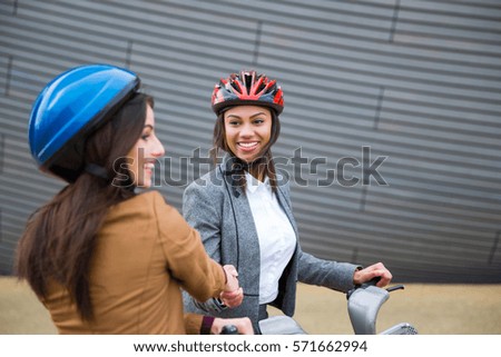 Two businesswomen shaking hands on bicycles in the city
