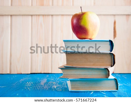Stack of books and fresh apple on wood board